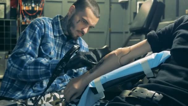 Taller con un artista tatuando a un hombre con una mano sintética — Vídeo de stock