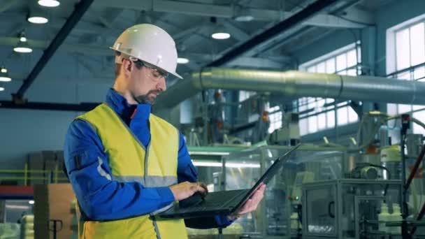 Un hombre de uniforme escribiendo en un portátil, trabajador de la fábrica . — Vídeos de Stock