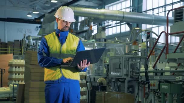 Persona trabaja con un ordenador portátil mientras está de pie en una sala de fábrica, la tecnología moderna . — Vídeos de Stock