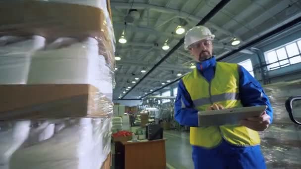 Mann tippt auf Tablet, während er einer Verpackungsmaschine beim Arbeiten zusieht. — Stockvideo