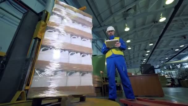 Una máquina envuelve cajas mientras una persona examina una producción automatizada de trabajo . — Vídeo de stock