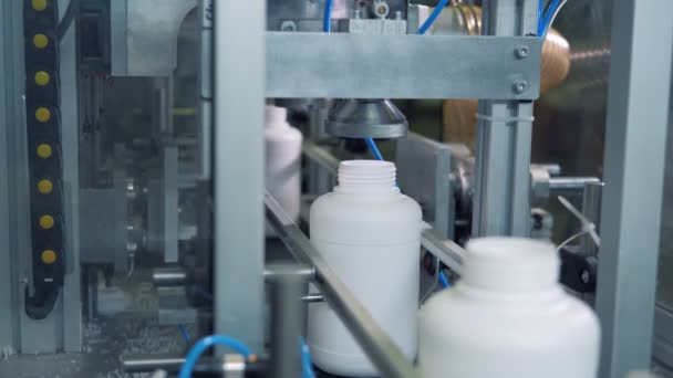Una máquina presiona botellas blancas mientras se mueven en una línea, producción moderna . — Vídeos de Stock