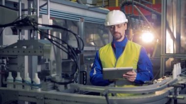 Bir kişi türleri fabrika konveyör çalışmalarını kontrol ederken bir Tablet.
