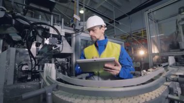 Mühendis bir bitki satırda otomatik ekipman hareketli şişe denetler.