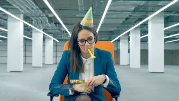 Uma funcionária explode uma bolacha de festa, usando um boné de comemoração. Conceito de aniversário maçante . — Vídeo de Stock