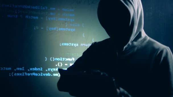 Hacker disfarçado está operando um tablet ao lado de uma parede com dados projetados — Vídeo de Stock