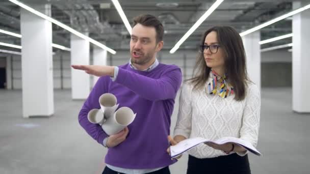 Engenheiros entram em uma sala e discutem um plano de trabalho, segurando plantas nas mãos . — Vídeo de Stock