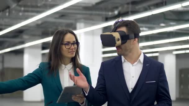 Male realtor in VR glasses talks to a woman with tablet in hands. — Stock Video