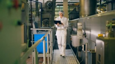 Kadın iş giysisi içinde fabrika ile bir dizüstü bilgisayar üzerinde yürüyor