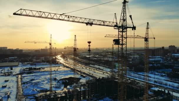 A paisagem urbana do pôr do sol com guindastes no lote de construção — Vídeo de Stock