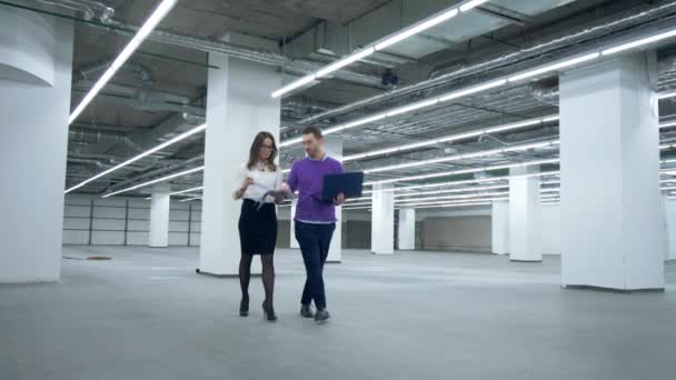 Ingenieros caminan en una habitación, trabajando con documentos y una computadora portátil . — Vídeos de Stock
