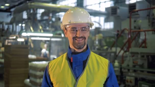 Trabajador de fábrica en un hardhat está sonriendo a la cámara — Vídeo de stock