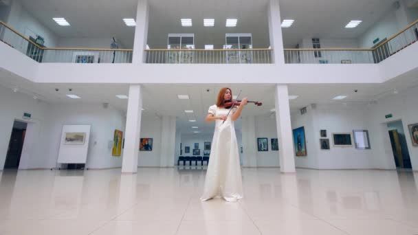 Een vrouw in witte jurk spelen viool in een museum. — Stockvideo