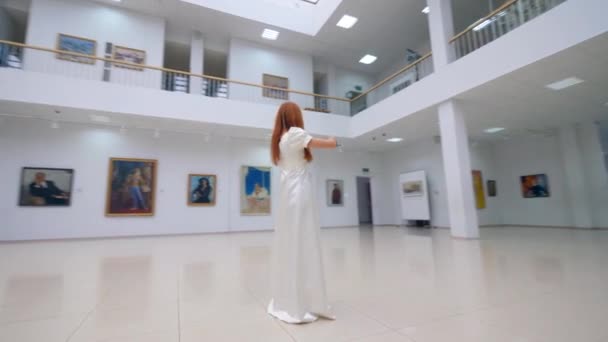 Professioneel muzikant in witte jurk speelt viool in museum met schilderijen. — Stockvideo