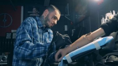Adam bir protez elde bir salonda bir dövme çizmek için bir makine kullanır.
