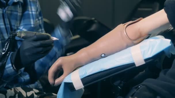 Tatuaje profesional que trabaja en una mano biónica de una persona discapacitada, equipo de tatuaje . — Vídeo de stock