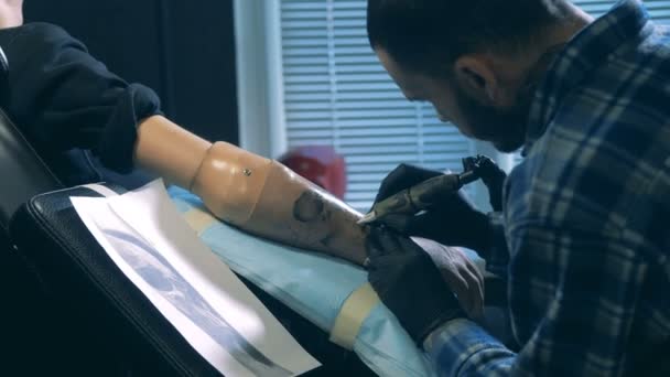 Trabajador de salón de tatuaje dibujando en un brazo protésico, prótesis biónica . — Vídeos de Stock