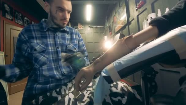 Tätowierer arbeitet mit behindertem Mann und zeichnet auf seiner prothetischen Hand. — Stockvideo