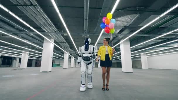 Een dame met ballonnen loopt met een cyborg langs de zaal — Stockvideo