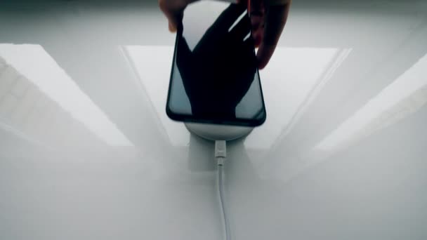 Концепція бездротової зарядки. Чоловік підключає чорний телефон до бездротового зарядного пристрою . — стокове відео