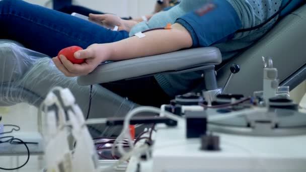 Person donates blood in a clinic, sitting in a chair near working machine. — Stock Video