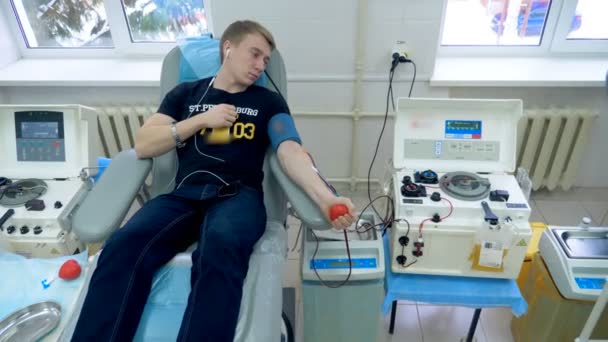 Young man uses a ball to pump blood in a donation center. — Stock Video