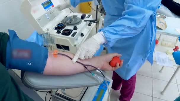 Doctor checks a working machine, while a volunteer donates blood in a center. — Stock Video