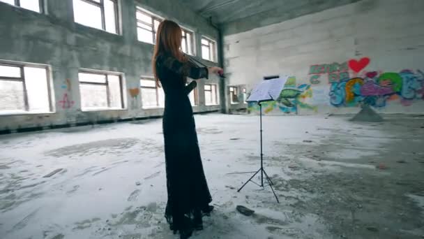 Mujer con un vestido tocando el violín en una sala descuidada — Vídeo de stock