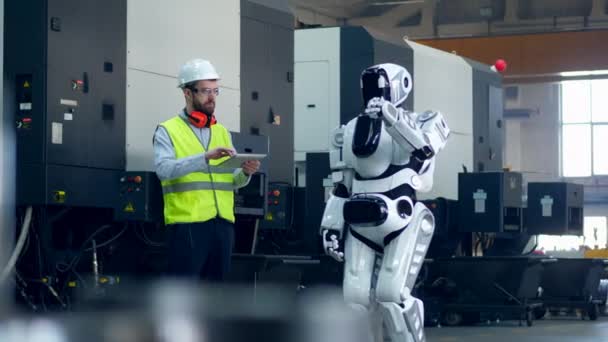 작업복을 입은 남자가 태블릿으로 로봇을 작동 — 비디오