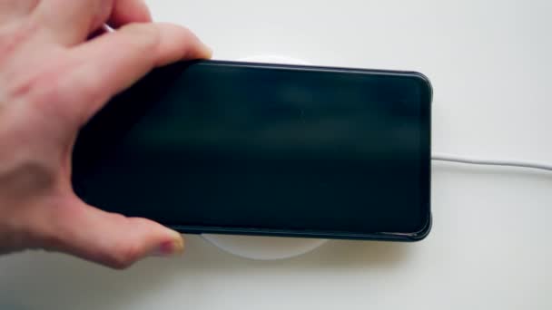 Een man zet een smartphone op een oplaadapparaat. Draadloos opladen concept. — Stockvideo