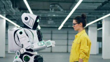 Genç kadın uzun robotların eline dokunuyor.