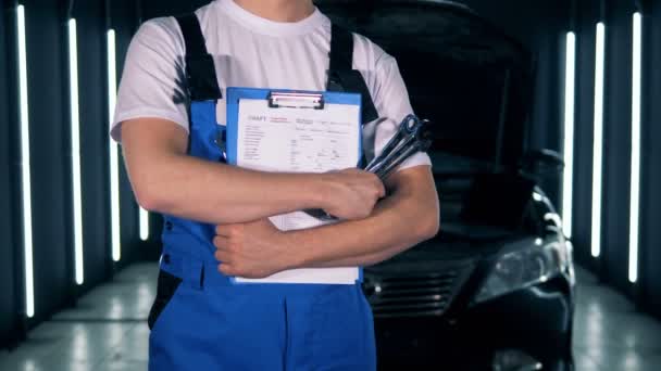 Service station en een mannelijke technicus staan met een Klembord en gereedschap. Auto service, auto reparatie concept. — Stockvideo