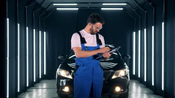 Hombre trabajador está tomando notas y sonriendo después de examinar un automóvil — Vídeo de stock