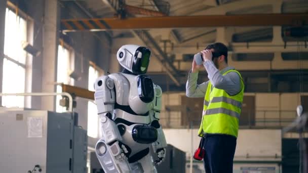 Um engenheiro usa equipamentos VR para controlar um dróide em uma fábrica . — Vídeo de Stock