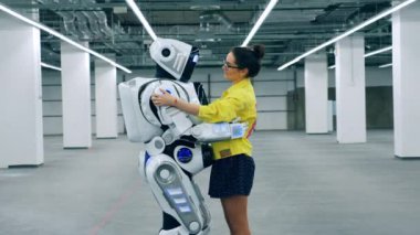 Genç bir kadın elinde bir cyborg tutuyor ve onunla konuşuyor.