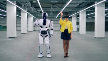 Young woman in VR-glasses and a robot are moving together