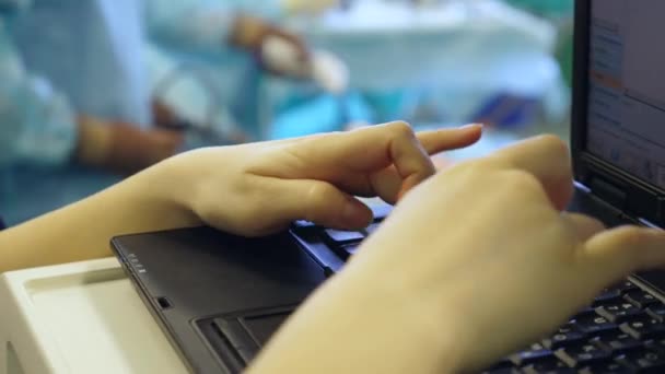 Een verpleegkundige werkt met een computer terwijl een chirurg een operatie uitvoert aan een patiënt. — Stockvideo