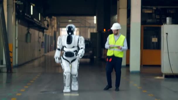 En ingenjör och en robot går längs fabriken — Stockvideo