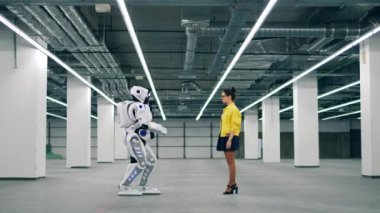 Bir robot bir kadına doğru yürür ve elini alır.