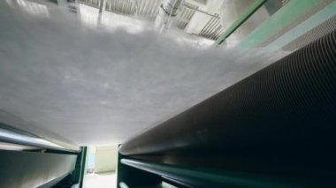 Metal rollers move a layer of polyester batting at a factory.