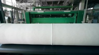 Fabrika konveyöründeki makaralara sarılmış sentetik malzeme.