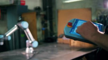 Bir adam tablette tip ler, çalışan bir robot kolunu kontrol ediyor.. 
