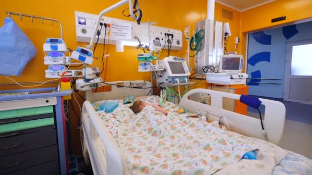 Sick child sleeps in bed in a hospital ward with medical machines. — Stock Video