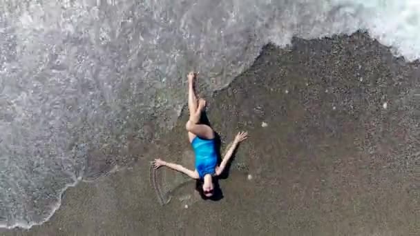 Женщина лежит на песке с морем, омывающим ее — стоковое видео