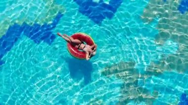 Bir bayan yüzme havuzunda yüzme halkası üzerinde yatıyor. Yaz tatillerinde kaygısız bayan.