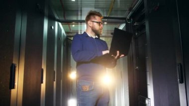 Bir adam bir sunucu odasında bir dizüstü bilgisayar ile duruyor