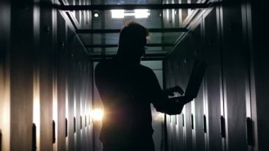 Sunucu odasında dizüstü bilgisayar üzerinde çalışan bir adamın silueti. Datacenter sunucu odası konsepti.