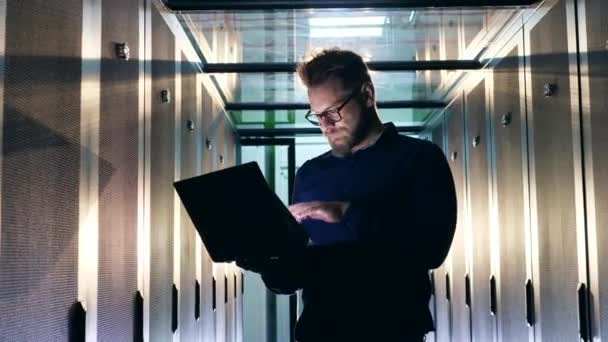 Un uomo sta navigando in un computer portatile in una sala server — Video Stock