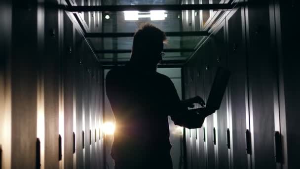 Sunucu odasında dizüstü bilgisayar üzerinde çalışan bir adamın silueti. Datacenter sunucu odası konsepti. — Stok video