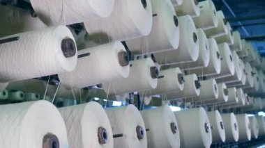 Beyaz iplikler makaralarla birlikte döner. Endüstriyel tekstil fabrikası.